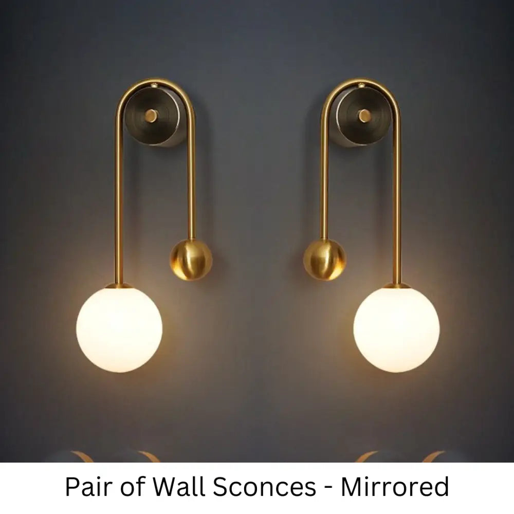 Pair of traditional gold wall sconces with curved metal arms and spherical frosted glass shades for elegant decor