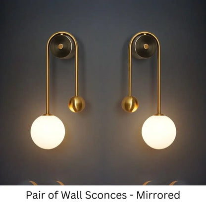 Pair of traditional gold wall sconces with curved metal arms and spherical frosted glass shades for elegant decor