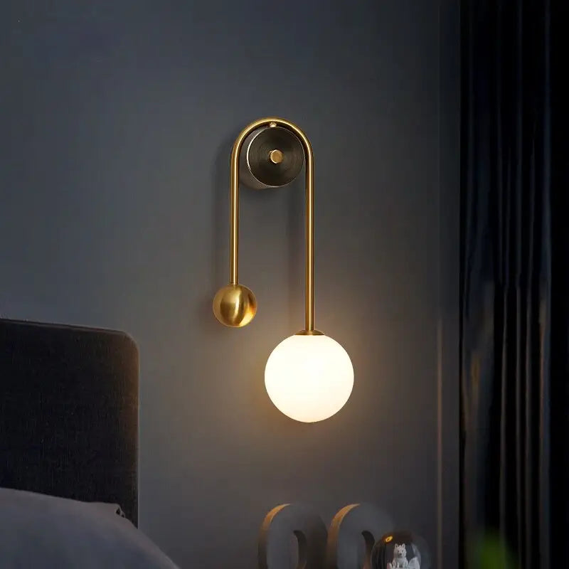 Traditional gold wall sconces with gold-toned curved arm, spherical frosted glass shade, and decorative smaller sphere