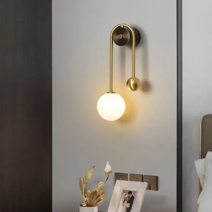 Traditional gold wall sconces with a curved arm and spherical glass globe in gold wall sconce design