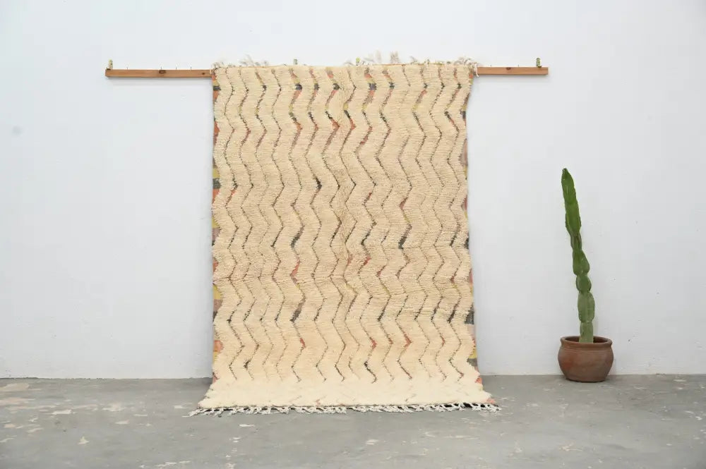 Cream-colored woven decorbites™ handmade traditional azilal rug with zigzag pattern and fringed edges on wooden rod