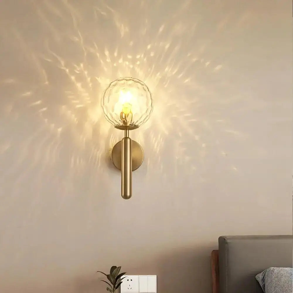 Brass-finished mynte wall sconce with textured clear glass globe emitting warm light for luxury decor