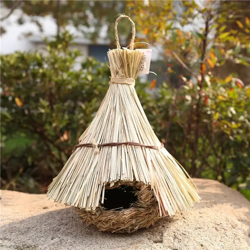 A rustic beige DecorBites natural grass bird cage with woven base and conical roof for a parrot nest