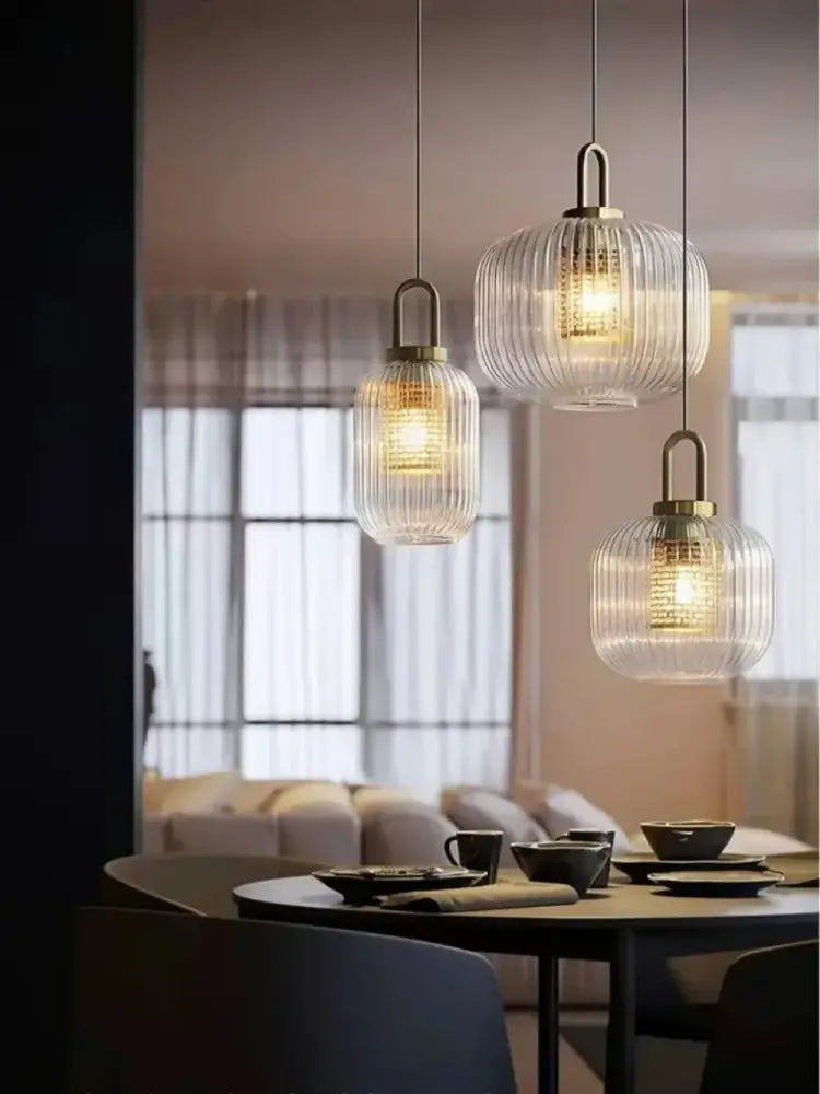 Three ribbed glass pendant lights with brass accents hanging above a dining table in a setting featuring a nordic deer head wall lamp