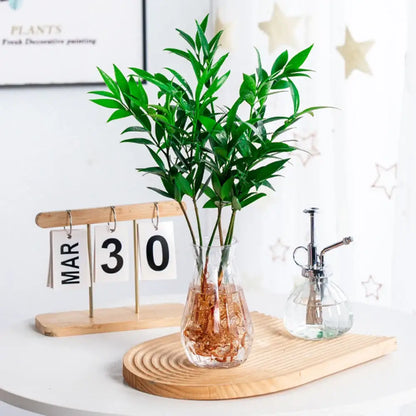 A clear glass nordic flower vase with a bulbous base holding vibrant green foliage for modern home decor