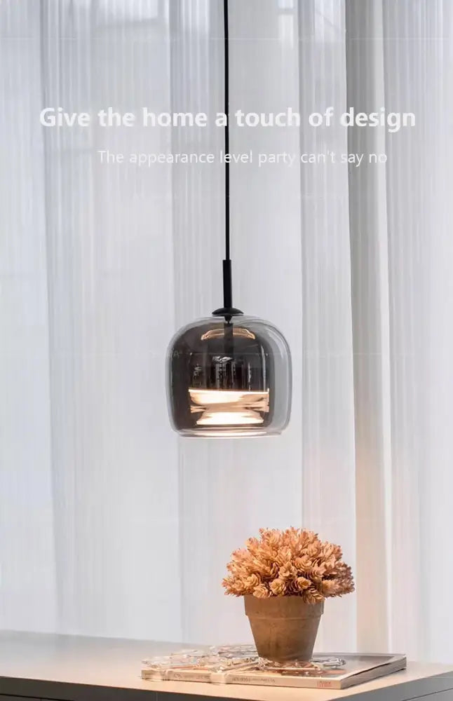 A sleek nordic glass led pendant light with smoked glass and black cord hangs above a small potted plant