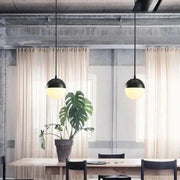 Black nordic industrial hanging pendant lights with frosted glass shades hang above wooden table by DecorBites