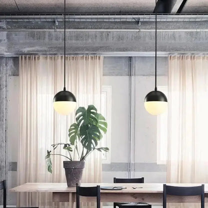Black nordic industrial hanging pendant lights with frosted glass shades hang above wooden table by DecorBites