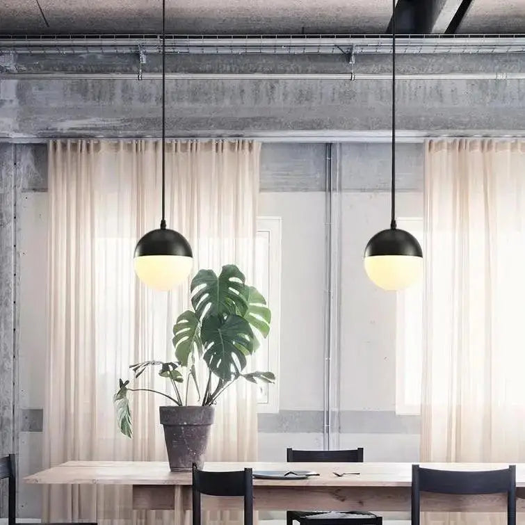 Black nordic industrial hanging pendant lights with frosted glass shades hang above wooden table by DecorBites
