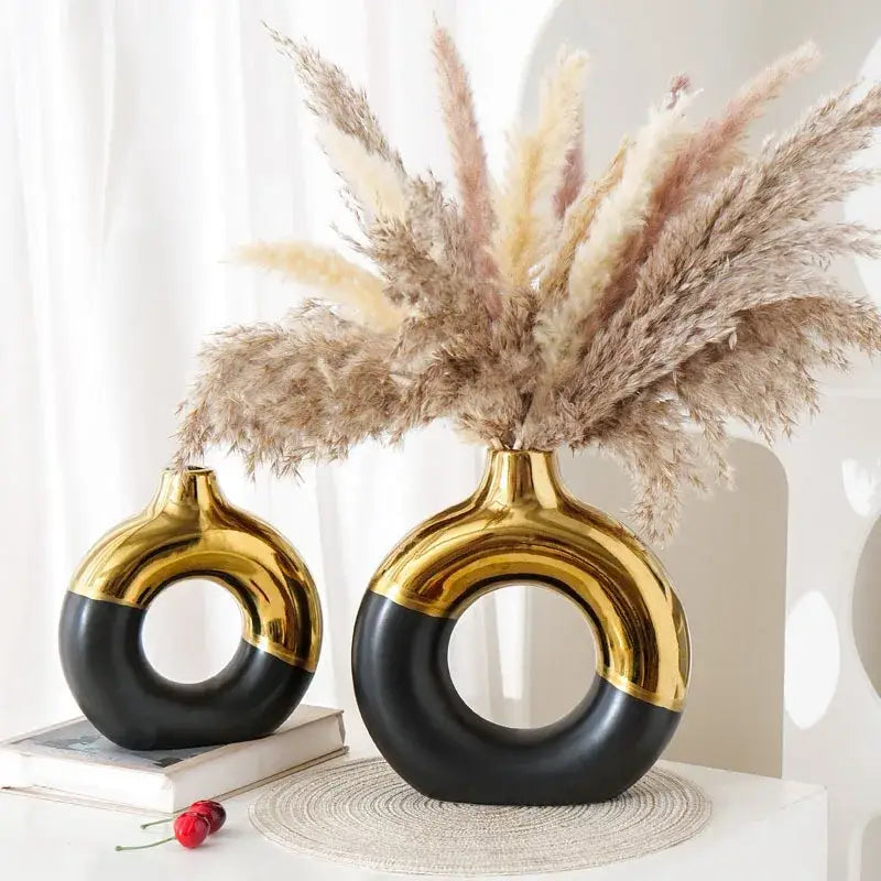Two glossy black and gold ceramic nordic style circle vases with distinctive ring design holding dried pampas grass