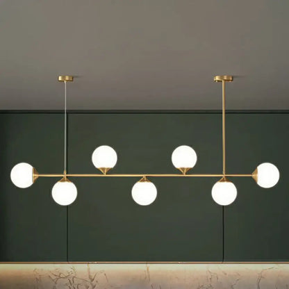 Modern gold-toned pendant light with five white opaline glass bulbs for minimalist dining room island lighting