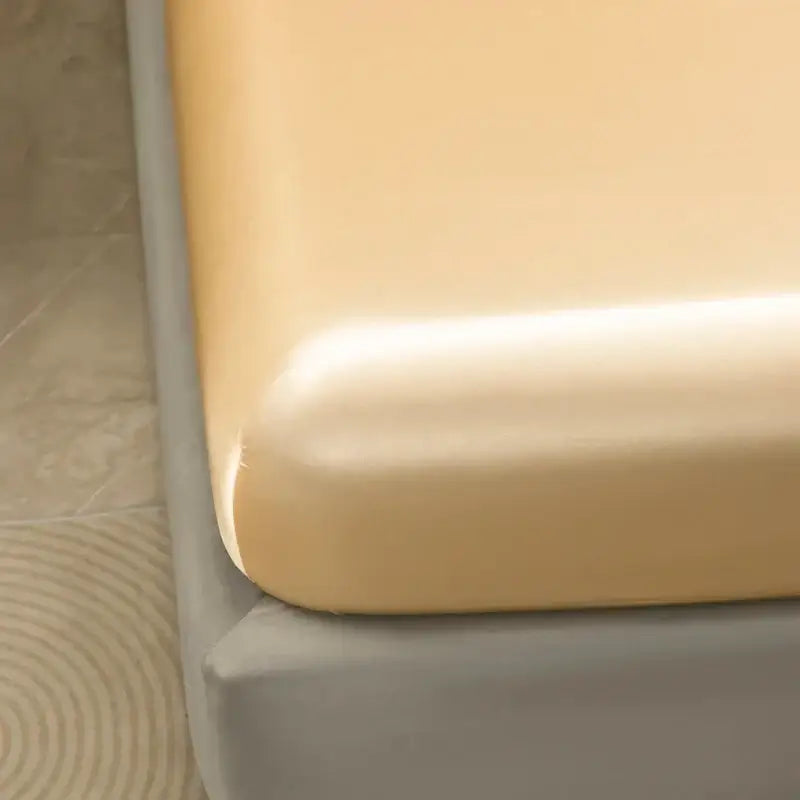 Cream-colored smooth textured mattress protector with snug fit from decorbites satin bedding set and flat sheet