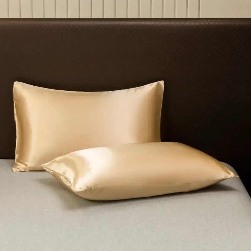 Two elegant gold satin pillowcases from the decorbites opulent satin bedding set against a dark headboard