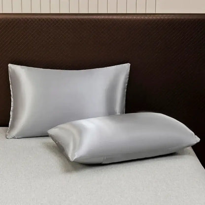 Two silver satin pillowcases from the decorbites opulent solid color satin bedding set on a bed with dark brown headboard