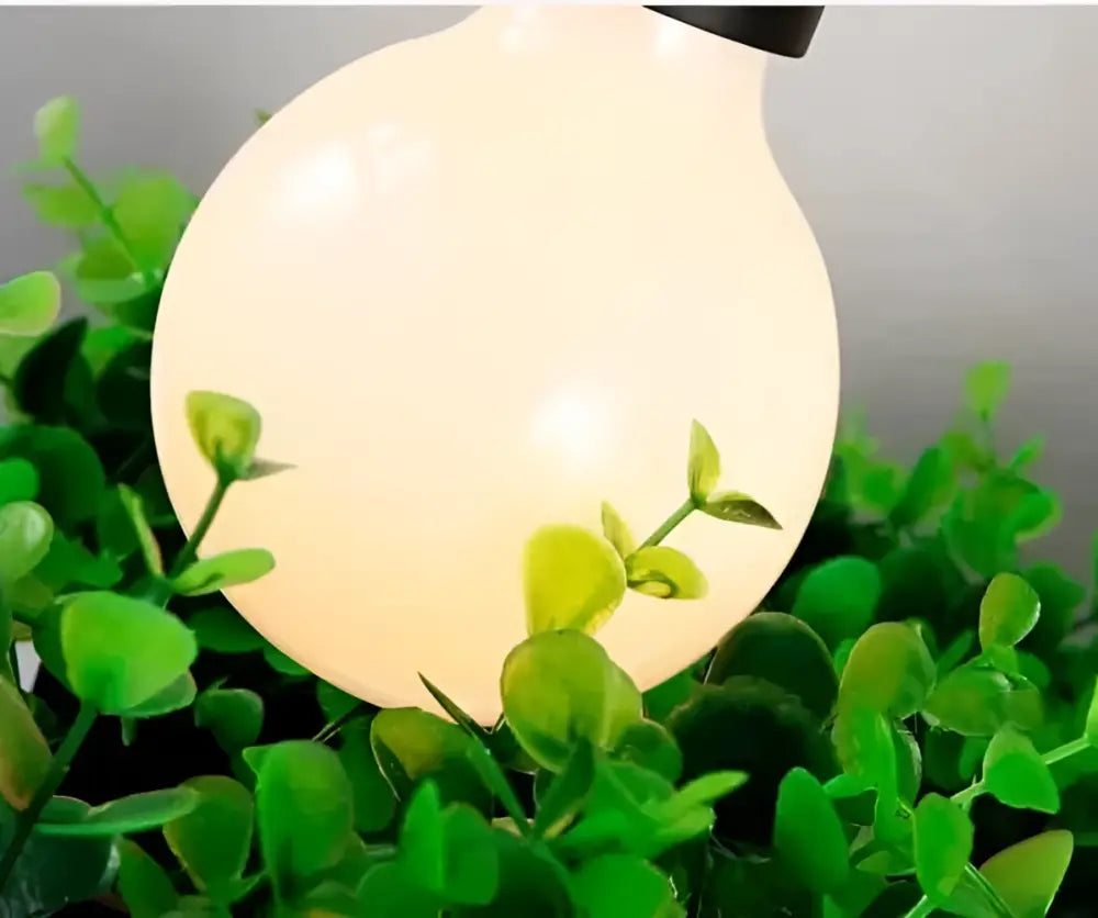 DecorBites planter light chandelier featuring a warm glowing globe led light bulb with black cap among green foliage