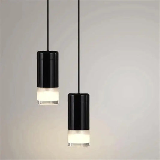 Two sleek black cylindrical decorbites plug-in hanging lights with frosted glass bases hang from thin cords