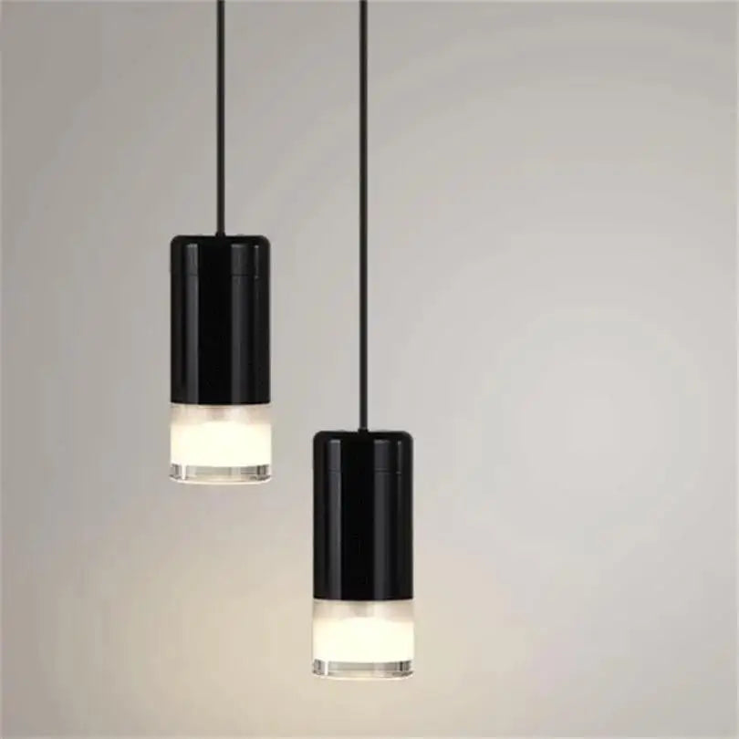 Two sleek black cylindrical decorbites plug-in hanging lights with frosted glass bases hang from thin cords