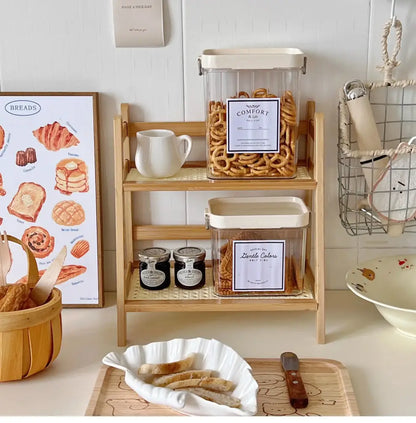 Clear plastic storage containers with cream lids and labels on a rattan 2-tier desktop organizer shelf