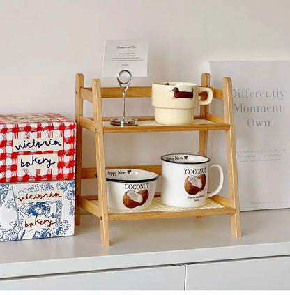 Light wood rattan two-tiered desktop organizer shelf with slatted design holding ceramic mugs and a card holder