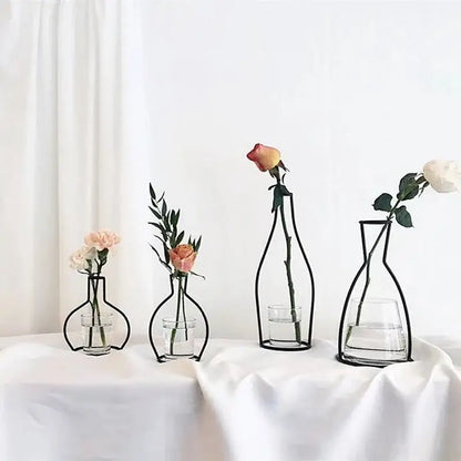 Black retro iron flower vase pot ornament with wireframe design and clear glass base holding single rose and greenery