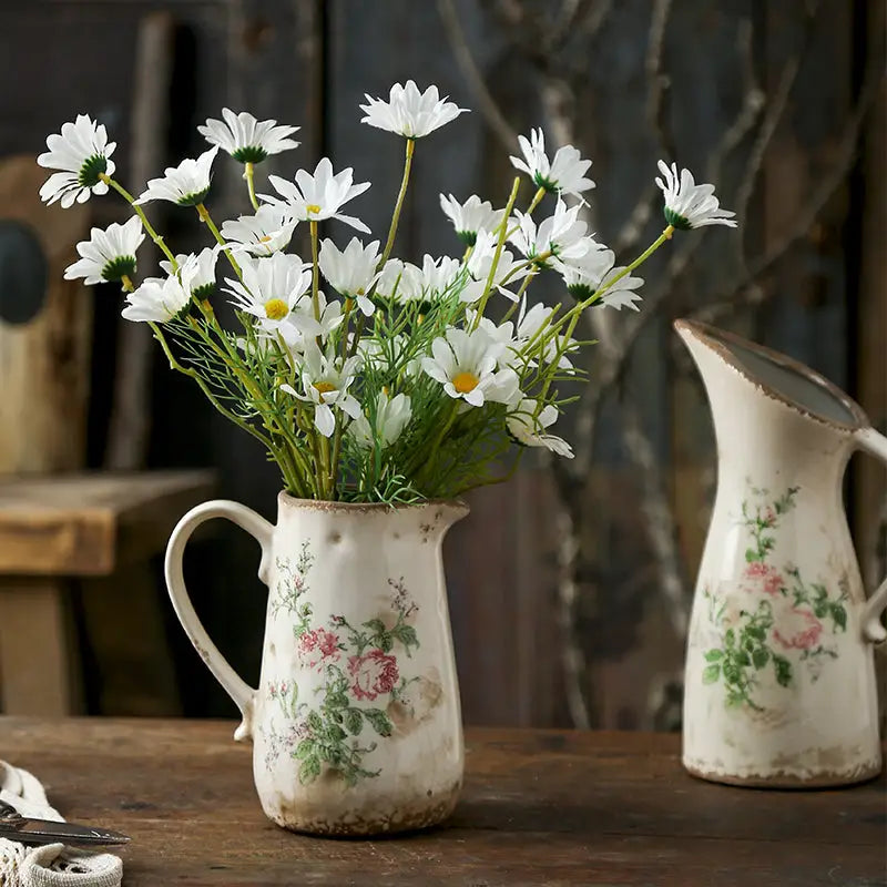 A rustic white ceramic vase with floral pattern and chipped glaze holding daisies in retro nordic ceramic style