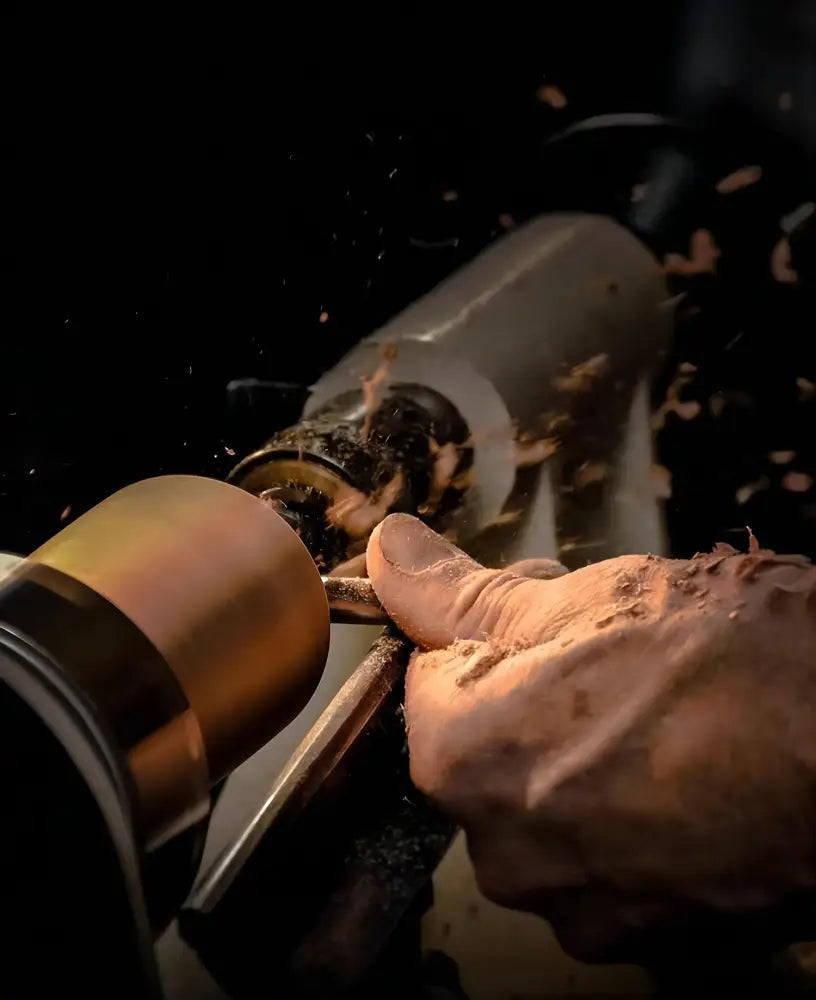 A hand guiding a woodturning tool shaping light brown wood for a walnut color DecorBites ceiling light