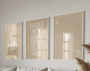 Set of three beige-framed wall art posters featuring minimalist white playing card designs and lucky you text by decorbites