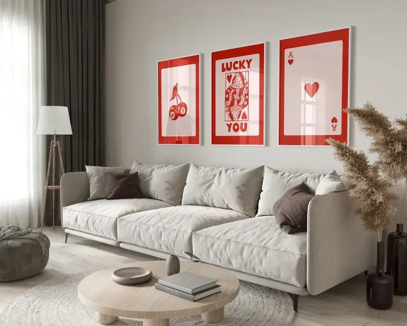 Three framed red and white queen of hearts wall art posters hang above a light gray sofa in a retro decor style