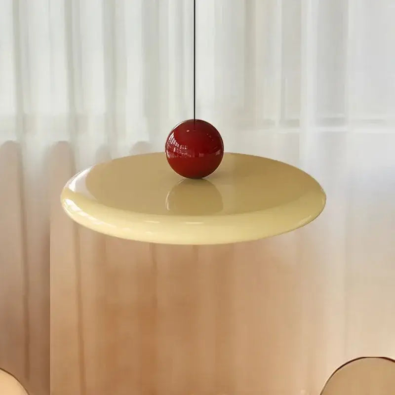 A glossy red spherical led pendant light from decorbites hangs above a pale yellow cream iron table