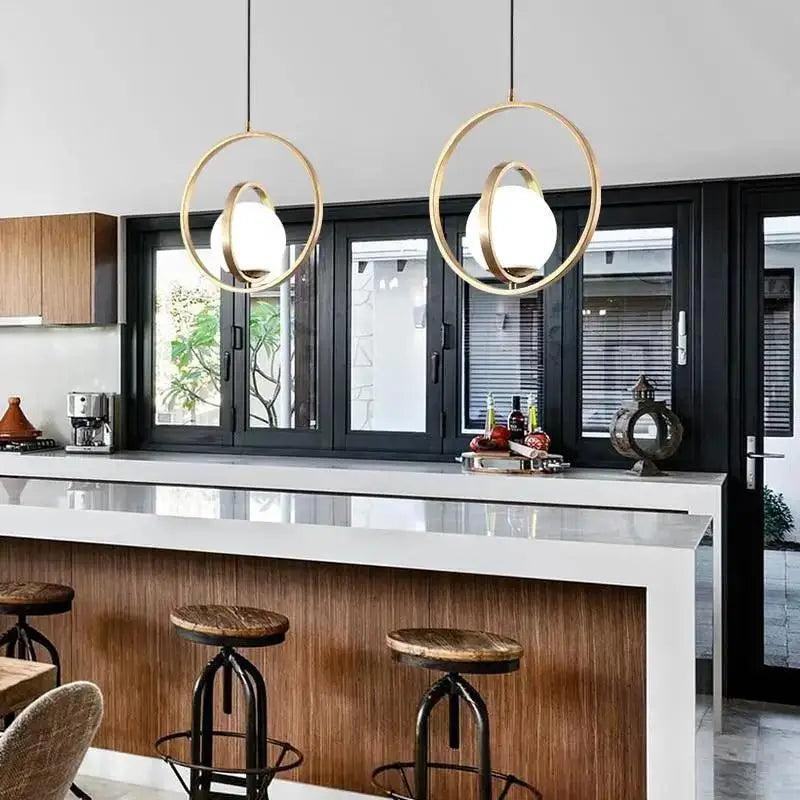 Two DecorBites™ rotating gold ring pendant lights with frosted glass globes hang above a kitchen island
