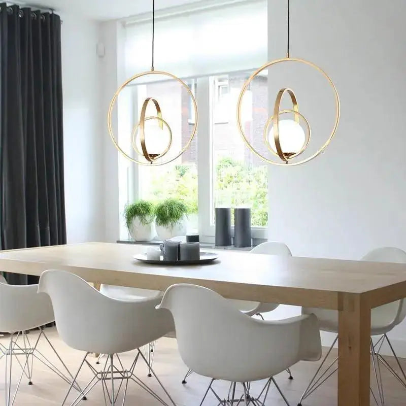 Two modern rotating gold ring pendant lights with frosted glass bulbs hang above a dining table by decorbites