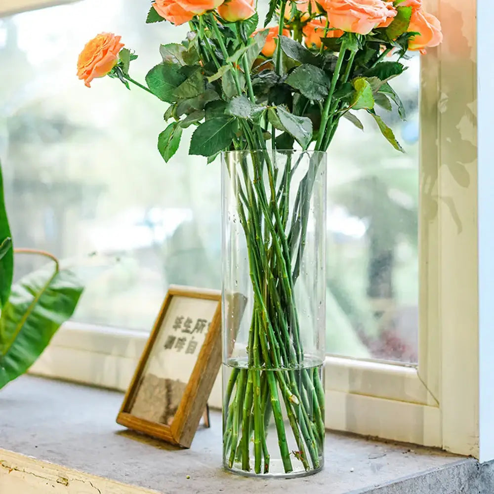 Decorbites™ shatterproof clear acrylic cylinder vase holding vibrant orange roses with green stems and leaves
