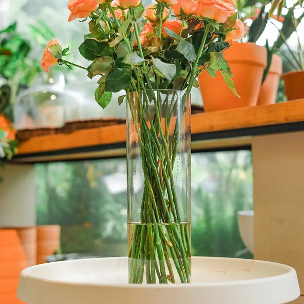 DecorBites™ shatterproof tall transparent acrylic flower vase holding a bouquet of vibrant peach roses with green stems