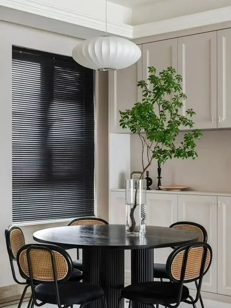 A sleek black round dining table with glossy finish and ribbed legs paired with a decorbites silk led pendant lamp