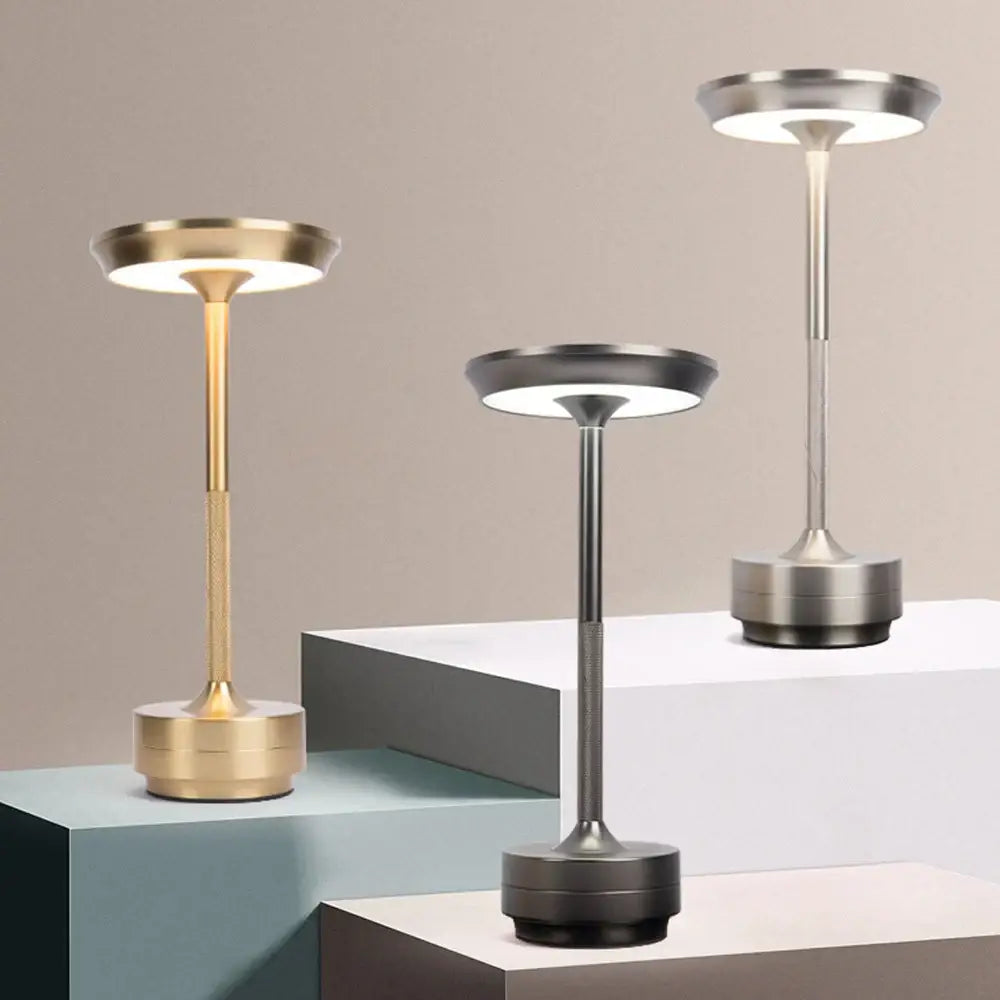 Three modern metallic DecorBites™ simple charging led desk lamps in gold silver and black on tiered pedestals
