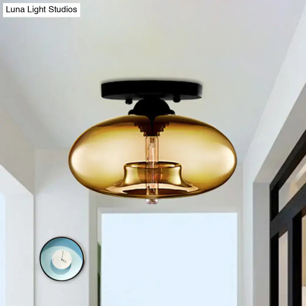 A sleek amber-tinted glass oval flush mount pendant light with black metal ceiling mount for hallway decor