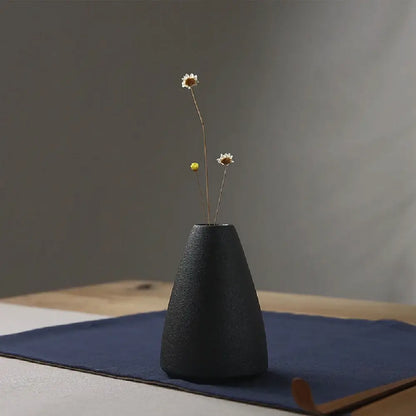 Black textured ceramic small vase holding dried white and yellow flowers for elegant japanese home decor