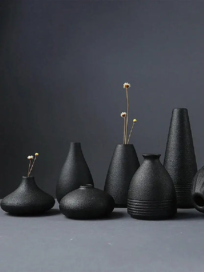 A collection of matte black ceramic small vases with textured surfaces holding dried flowers for elegant japanese home decor