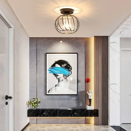 Black-framed artwork of woman with blue paint across eyes on gray marble wall near decorbites small metal cage ceiling light