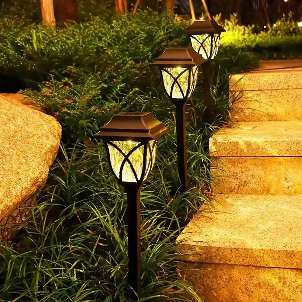 Black solar lawn lights with ornate lantern-style glass panels emitting a warm glow for outdoor garden use