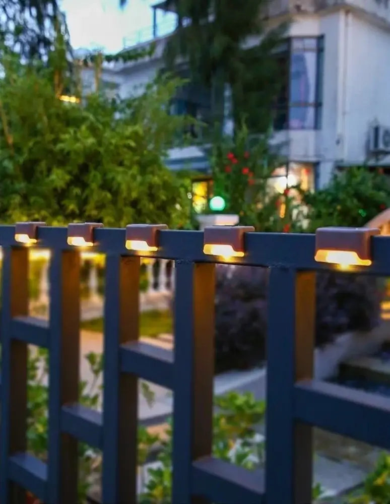 DecorBites solar led outdoor stair lights with amber glow and matte brown casing mounted on dark blue metal fence