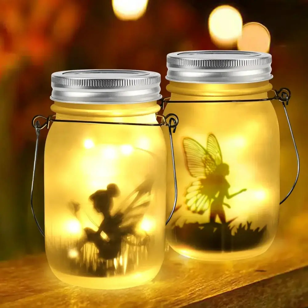 Two illuminated glass solar mason jar lanterns with silver lids and fairy silhouette led lights for garden decoration
