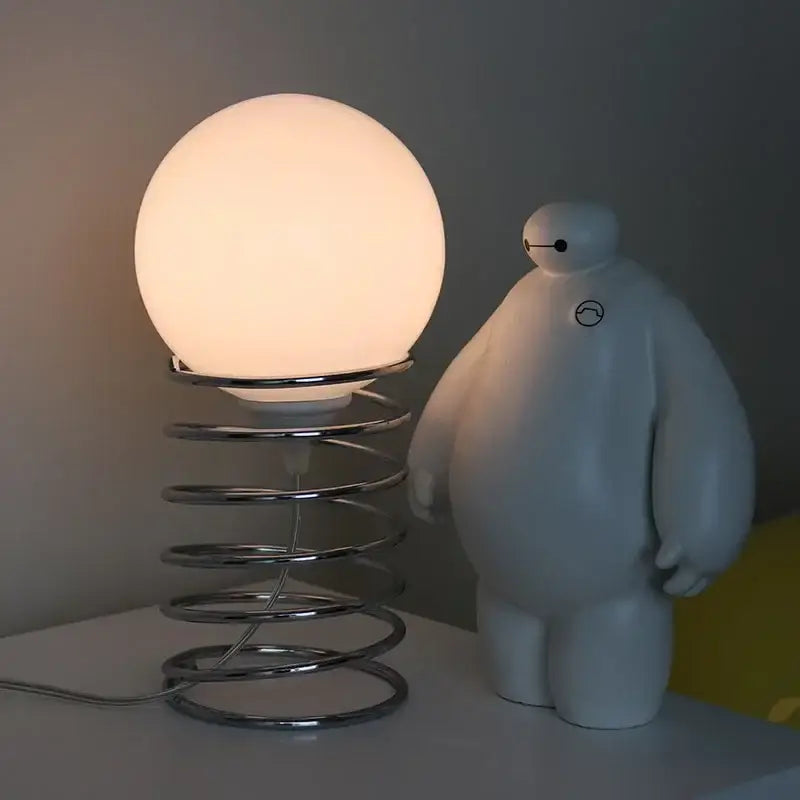 A glowing spherical glass table lamp with a chrome spring base from decorbites bauhaus furniture collection