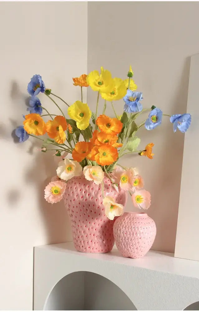 Pink ceramic flower vase with cartoon strawberry pattern filled with vibrant yellow orange and blue artificial poppies