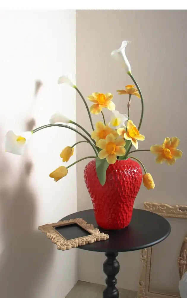 A vibrant red cartoon strawberry flower vase by decorbites holding white calla lilies and yellow daffodils for home décor
