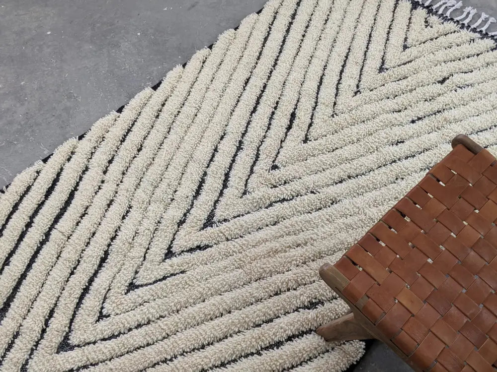 Cream-colored plush tapis beni ouarain rug with bold black zigzag patterns and fringed edge by decorbites