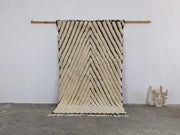 Cream-colored textured wool tapis beni ouarain with bold black zigzag stripes and fringed edges by decorbites