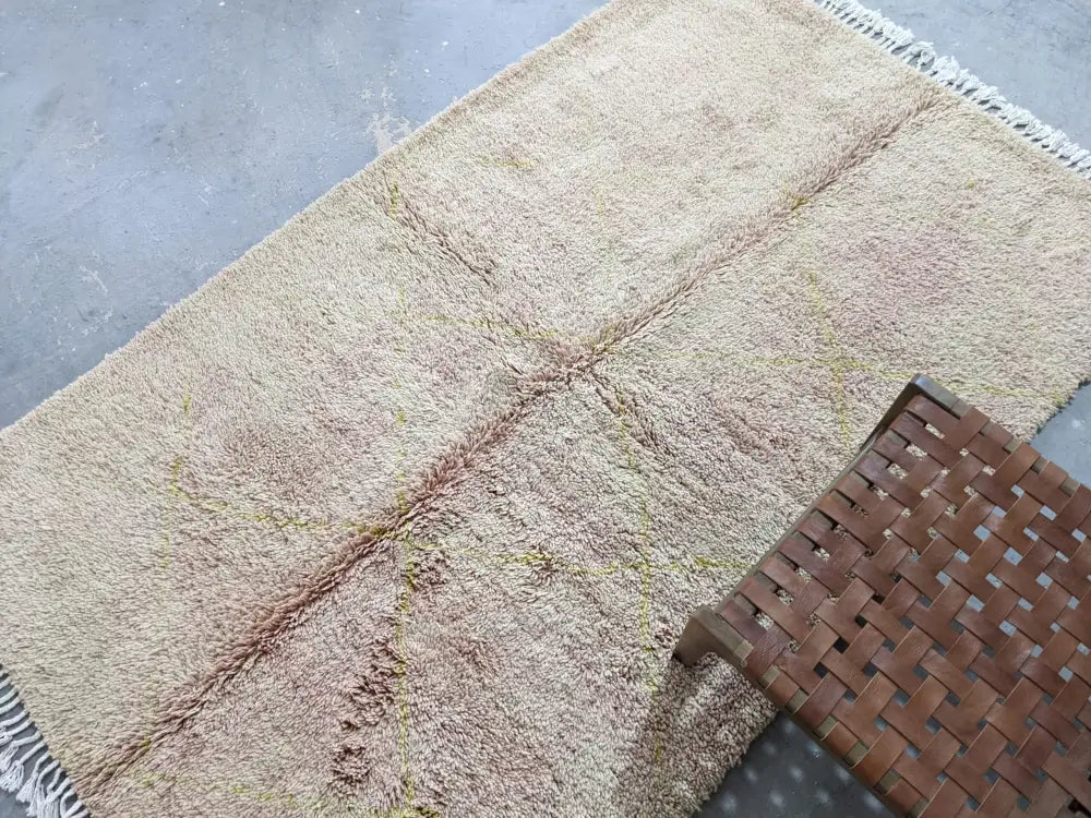 Beige shaggy wool tapis beni ouarain with fringed edges and subtle faded pinkish brown patches by decorbites