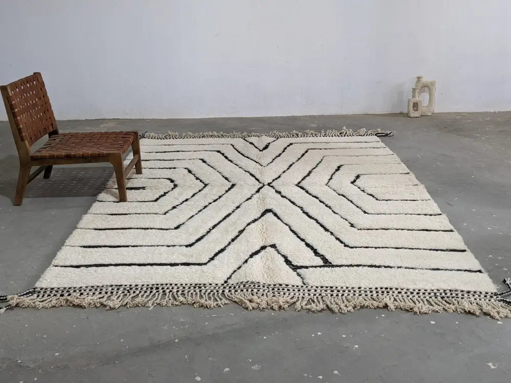 Cream-colored wool tapis beni ouarain with bold black geometric patterns and fringed edges by DecorBites™