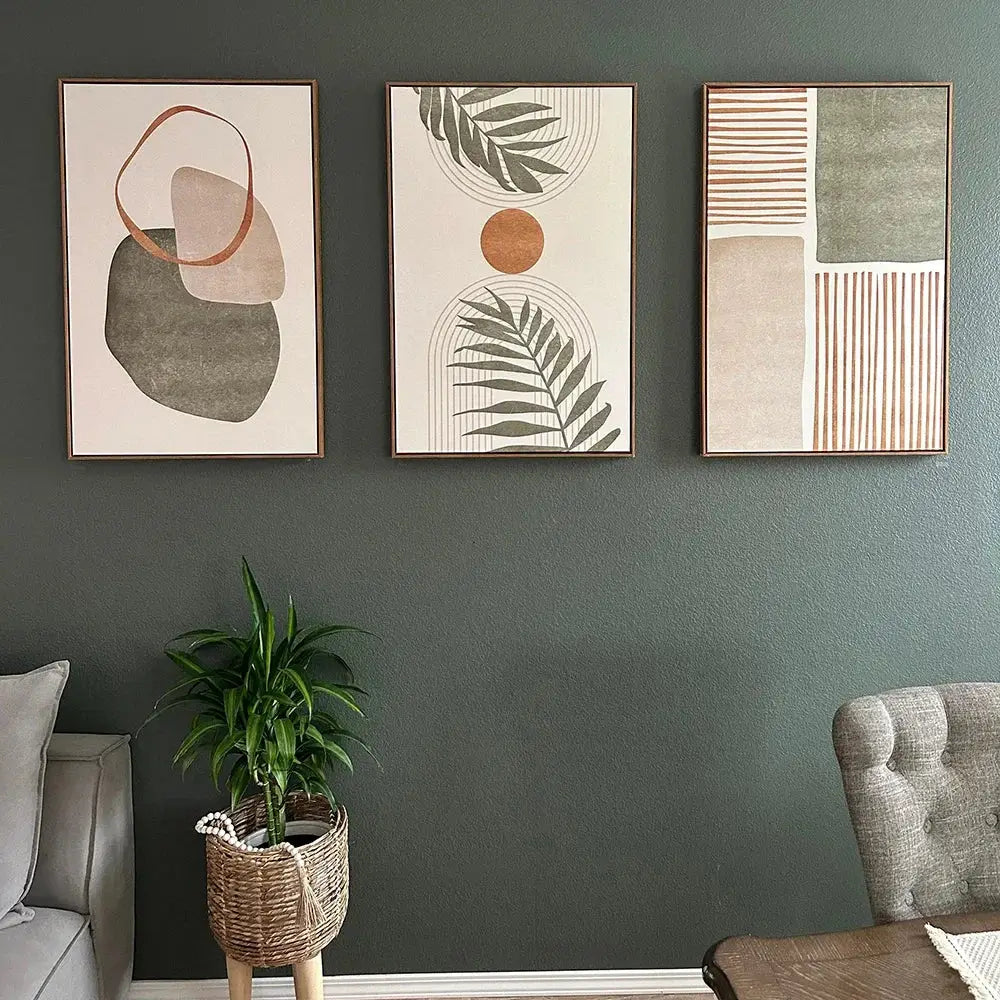 Three framed abstract shapes canvas wall art with earthy tones featuring tropical leaves on a dark green wall by decorbites